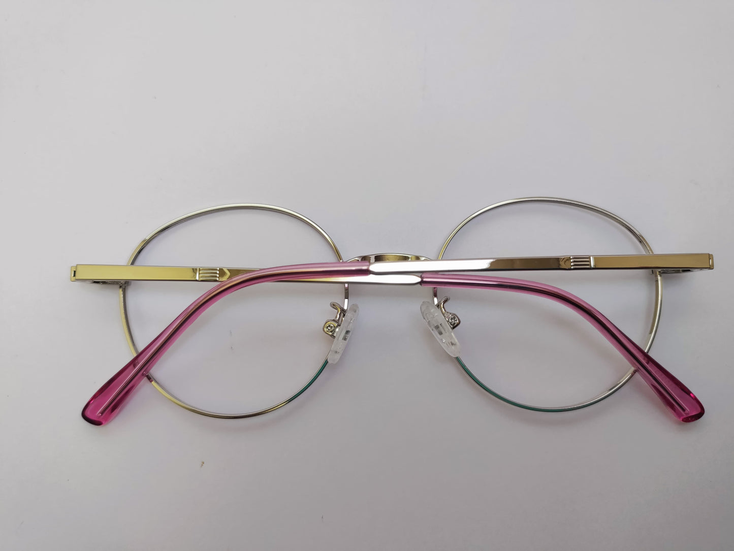 Round eyeglasses with gold and pink frames on a light gray background