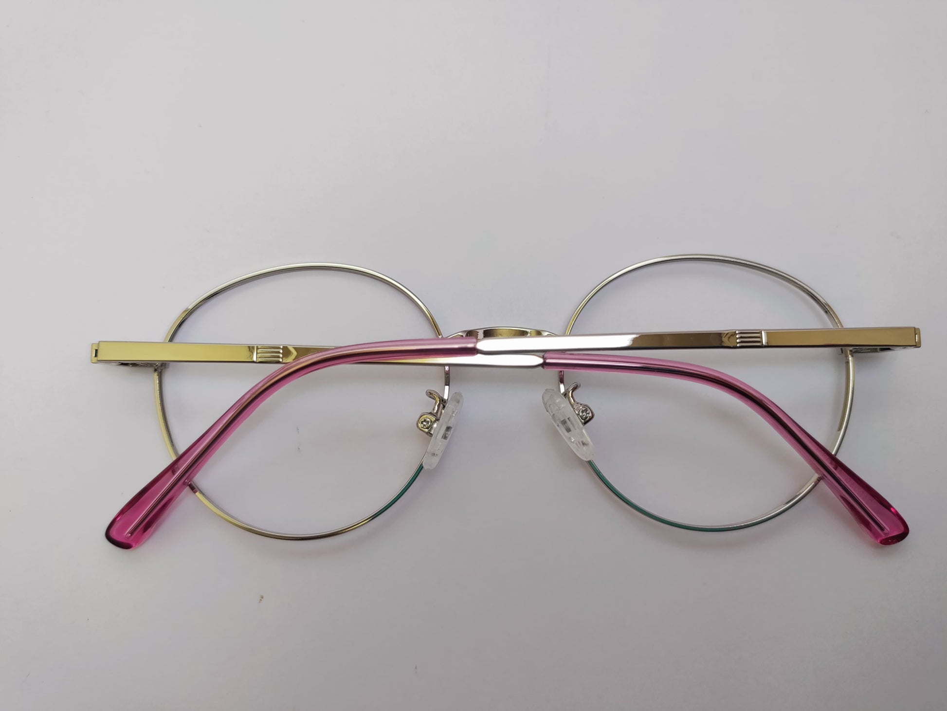 Round eyeglasses with gold and pink frames on a light gray background